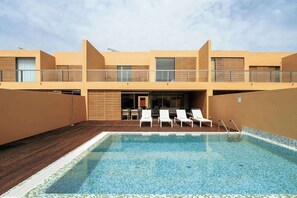 A modern hotel with a rooftop pool, lounge chairs, and a covered terrace.
