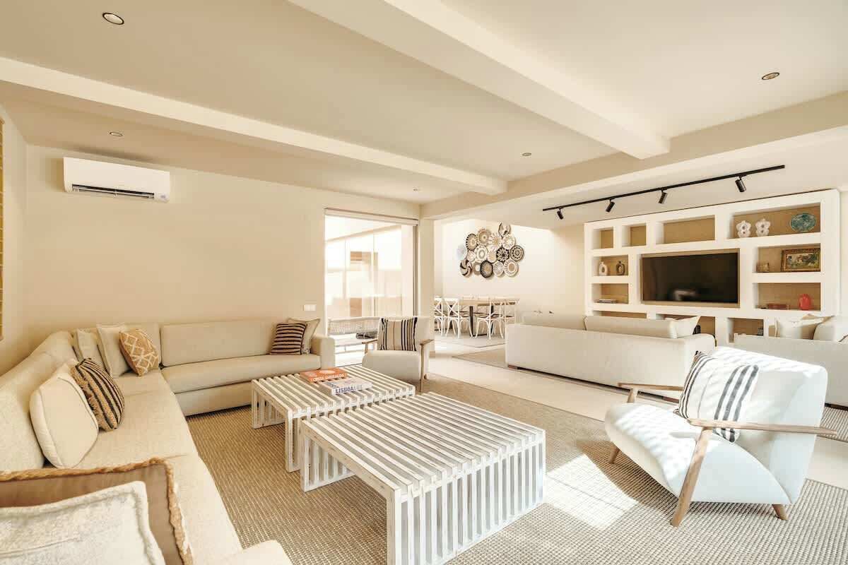 A modern living room with a sofa, coffee table, and armchair, a TV, and a wall-mounted shelf with decorative items.