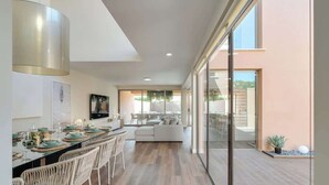 A modern interior with a dining area, a sofa, and a glass door leading to an outdoor space. - 4BR Villa w/ Private Pool | Salgados | DA’Home (Guia)