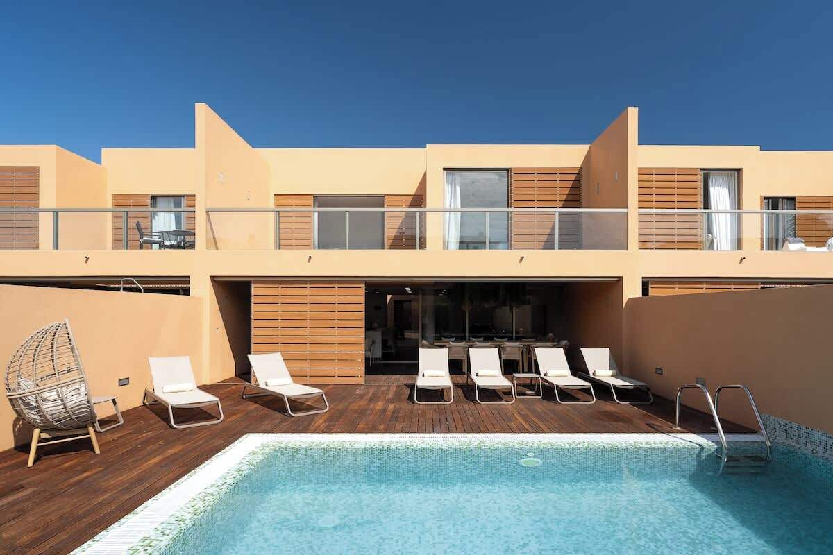 A modern hotel with a rooftop pool, lounge chairs, and a dining area.