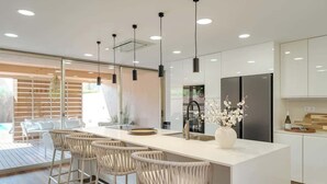 A modern kitchen with a white island, bar stools, pendant lights, and a large refrigerator. - 4BR Villa w/ Private Pool | Salgados | DA’Home (Guia)