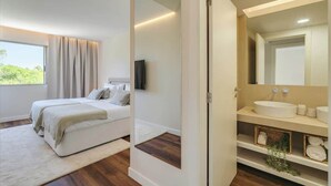 A bedroom with a bed, a TV, a bathroom with a sink and mirror, and a view of greenery outside. - 4BR Villa w/ Private Pool | Salgados | DA’Home (Guia)