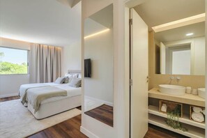 A bedroom with a bed, a TV, a bathroom with a sink and mirror, and a view of greenery outside. - 4BR Villa w/ Private Pool | Salgados | DA’Home (Guia)