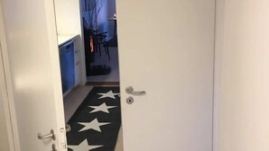 Un pasillo con una puerta que da a una habitación. Hay una alfombra negra con estrellas blancas en el suelo.