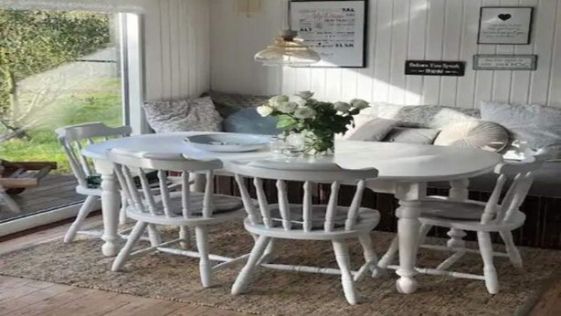 A cozy room with a round table and white chairs, a sofa with cushions, and a small table with a vase of flowers. - 5 Star Holiday Home in Dronningmolle (Dronningmolle)