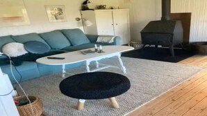 A living room with a sofa, a coffee table, a black ottoman, a fireplace, and a cabinet. - 5 Star Holiday Home in Dronningmolle (Dronningmolle)