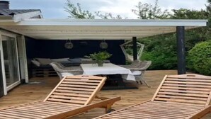A covered outdoor area with a dining table and chairs, a hammock, and two wooden loungers. - 5 Star Holiday Home in Dronningmolle (Dronningmolle)