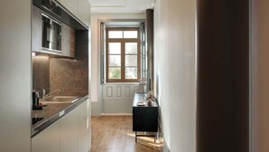 A narrow hallway with a kitchen area on one side, featuring a window and a small table with a vase.