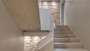 A modern staircase with a stone wall at the bottom and a concrete beam overhead.