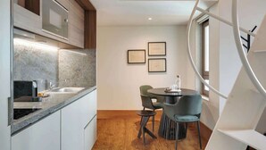 A modern kitchen with a built-in stove, a sink, and a dining area with a round table and chairs. There are framed certificates on the wall and a spiral staircase to the right. - Republica 144 Apartamentos by DA'Home (Porto)