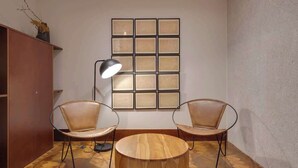 A modern room with a wooden floor, two leather chairs, a round wooden table, a floor lamp, and a wall with framed artwork. - Republica 144 Apartamentos by DA'Home (Porto)