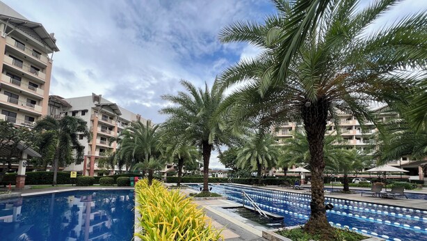 A swimming pool area with a clear sky, palm trees, and multi-story buildings in the background. - Japan Vibe 2-bedroom condo with Veranda Pool View and AC in vibrant Pasig (Pasig)