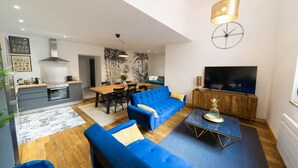 Ett modernt vardagsrum med en blå soffa, en matplats, ett kök och en TV.