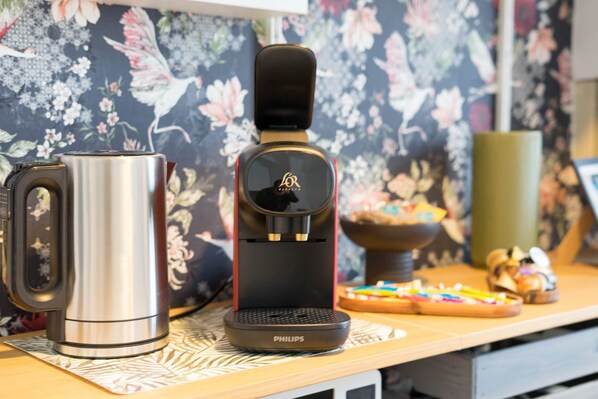 A coffee maker and a kettle on a wooden table with a floral wallpaper background. - Résidence Bardiaux - Chez Sauge (Vichy)