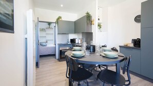 A compact kitchen with modern appliances, a dining area with a round table and chairs, and a bed in the adjacent room. - Résidence Bardiaux - Chez Mélèze (Vichy)