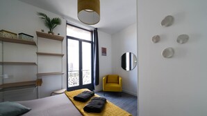 A modern hotel room with a bed, a yellow chair, a large window, and a mirror on the wall. - Résidence Bardiaux - Chez Mélèze (Vichy)