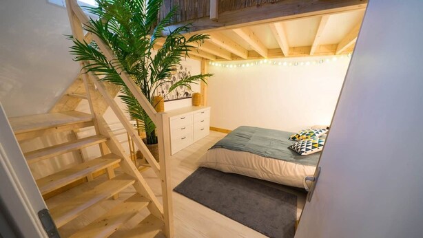 Une chambre avec un escalier en bois, un lit, une table de chevet et une plante en pot.