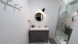 A modern bathroom with a white vanity, a round mirror, and a glass shower enclosure. - Résidence Thermale - Chez Helder, the Suite 💎 (Vichy)