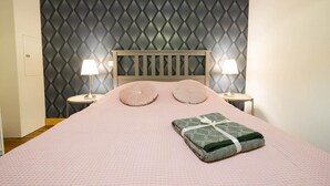 A neatly made bed with a pink bedspread and pillows, two bedside lamps, and a patterned wallpaper. - Résidence Thermale - Chez Helder, the Suite 💎 (Vichy)