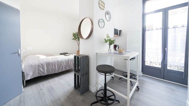 A modern bedroom with a bed, a desk with a chair, a small plant, and a window with a view.