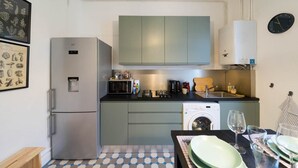 A compact kitchen with a refrigerator, microwave, stove, and washing machine. - Résidence Carnot - Chez Klein (Vichy)