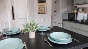 A dining area with a black table set with light blue plates, wine glasses, and cutlery. There is a small potted plant on the table. - Résidence Carnot - Chez Klein (Vichy)
