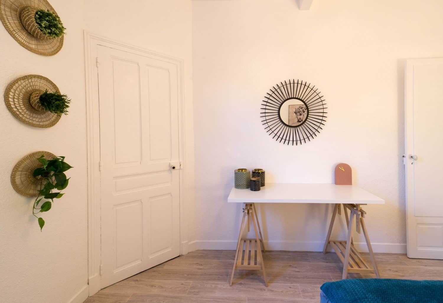 Una habitación con una puerta blanca, una mesa blanca y un taburete pequeño, además de un adorno en la pared.
