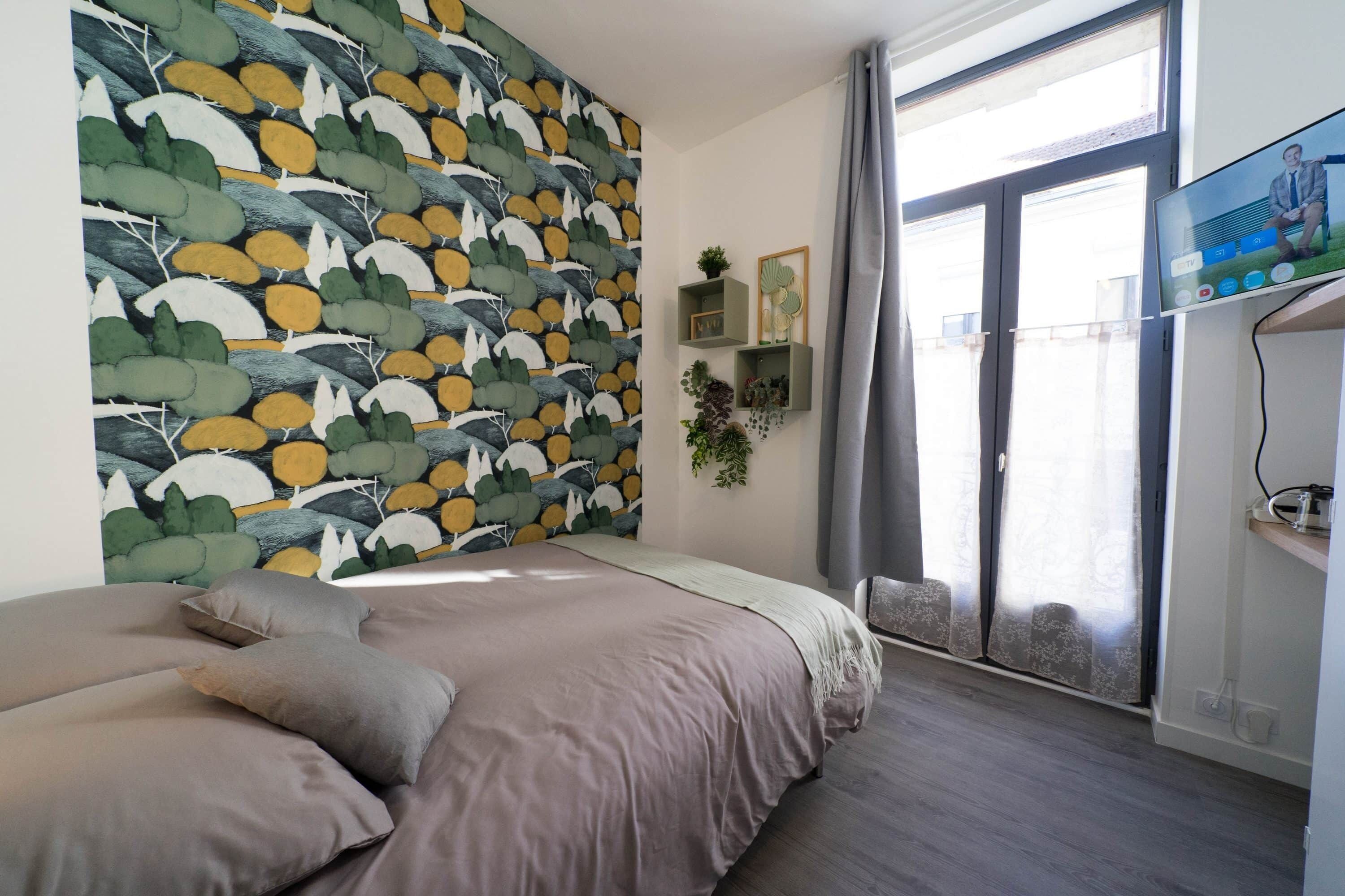A bedroom with a bed, a wall with a leaf pattern, a TV, and a window with curtains.