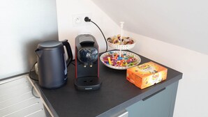 A kitchenette with a coffee maker, kettle, and a bowl of colorful items on the counter.