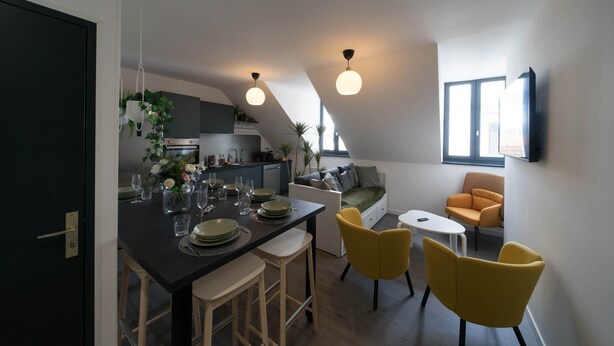 A modern kitchen with a dining area, yellow chairs, and a TV mounted on the wall.