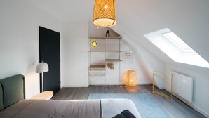 A modern bedroom with a skylight, a bed, a bedside lamp, a shelf with decorative items, and a hanging light fixture.