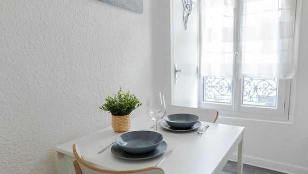 A white dining table with two blue plates, a knife, and a fork. There is a potted plant on the table. - Résidence Carnot - Chez Majorelle (Vichy)