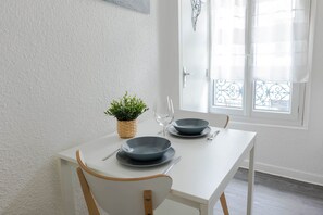 Une table de salle à manger blanche, avec deux assiettes bleues, un couteau et une fourchette. On peut voir une plante en pot sur la table.