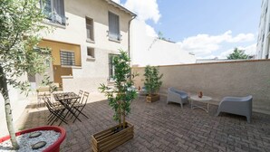 A courtyard with outdoor seating, potted plants, and a building with a white facade and shutters. - Résidence Carnot - Chez Majorelle (Vichy)