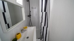 A bathroom with a white sink, mirror, and shower. - Résidence Carnot - Chez Majorelle (Vichy)