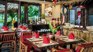 Een restaurant met houten tafels en stoelen, rode servetten en een tropische inrichting.