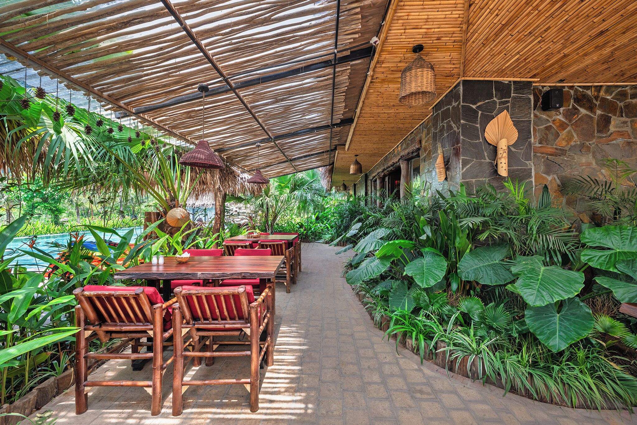 A covered outdoor dining area with tables and chairs, surrounded by lush tropical plants.