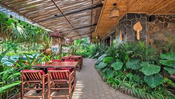 A covered outdoor dining area with tables and chairs, surrounded by lush tropical plants.