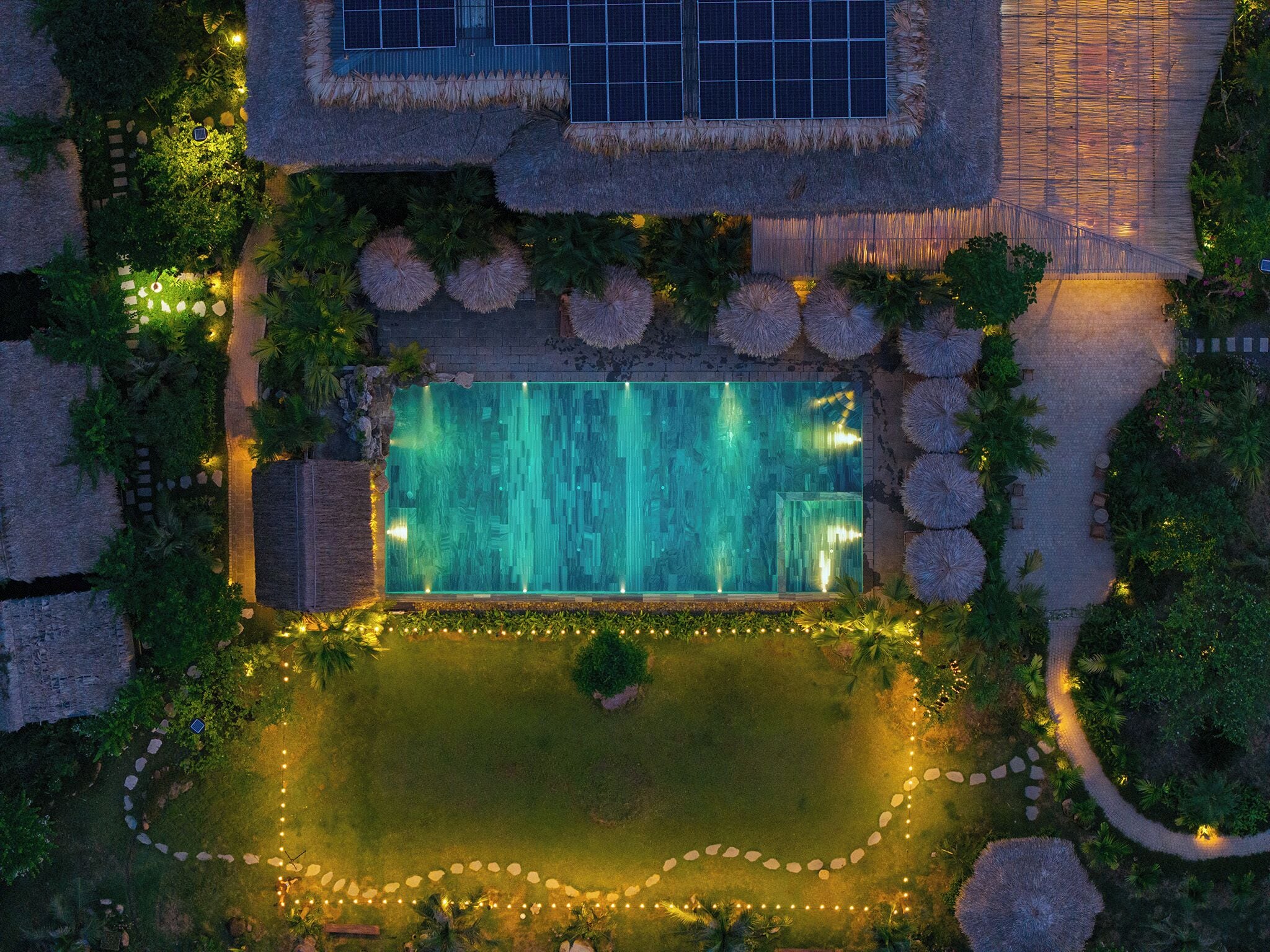 An aerial view of a resort with a swimming pool, lush landscaping, and solar panels.