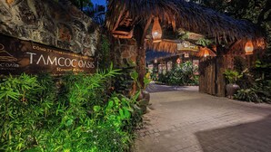 A tropical resort entrance with a thatched roof, a sign for Tamcooc Oasis Resort & Spa, and lush greenery. - Tam Coc Oasis Resort & Spa (Nam Hoa Lu)