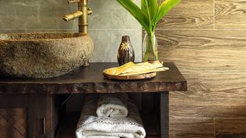 A bathroom with a stone sink, a wooden vanity, towels, and a vase with flowers.