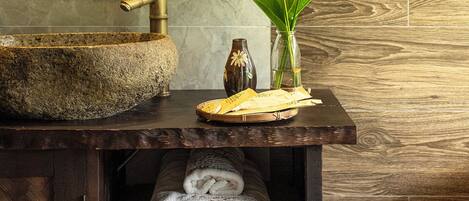 A bathroom with a stone sink, a wooden vanity, towels, and a vase with flowers.