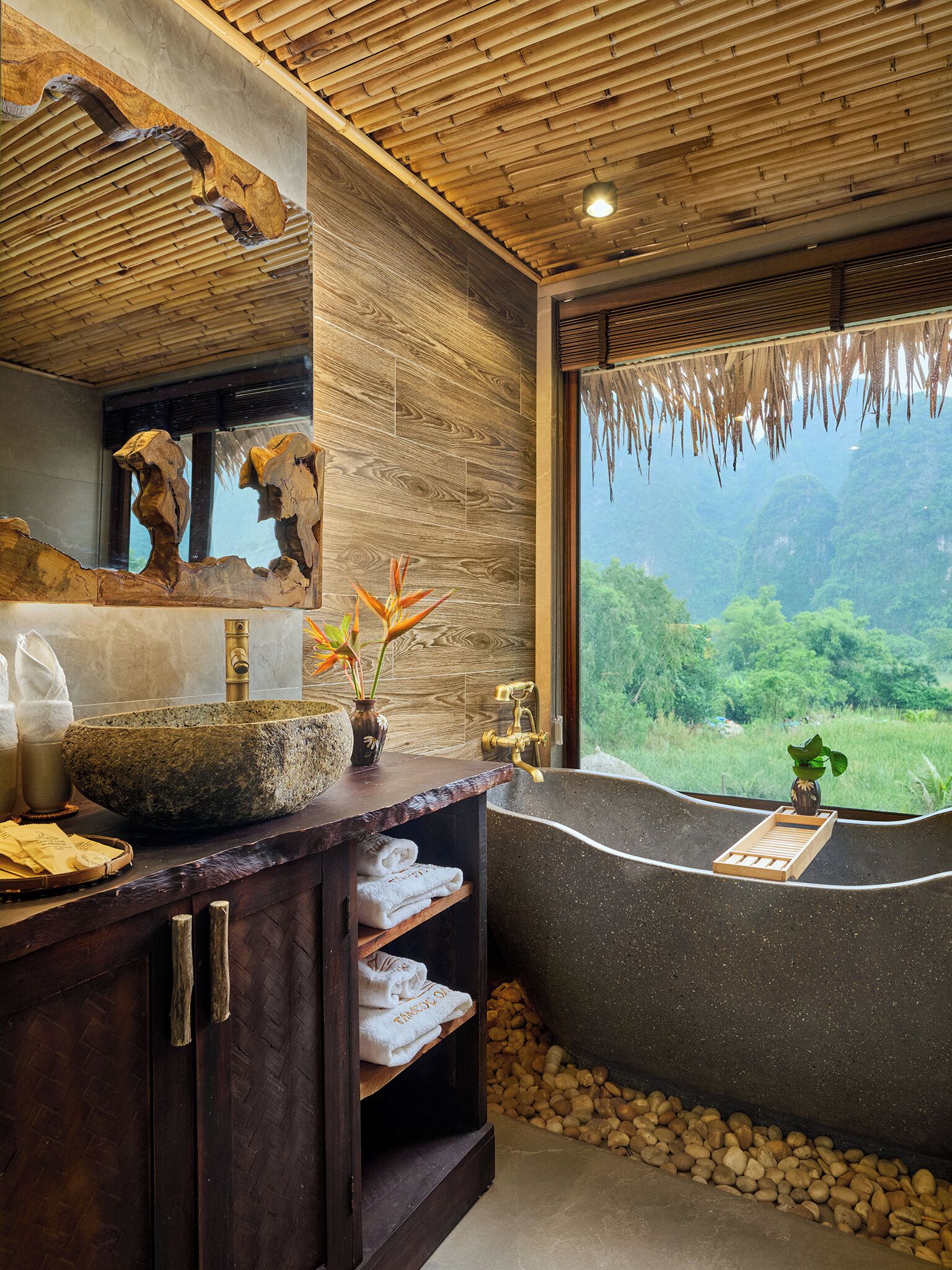 A bathroom with a stone sink, wooden vanity, and a bathtub with a view of greenery.