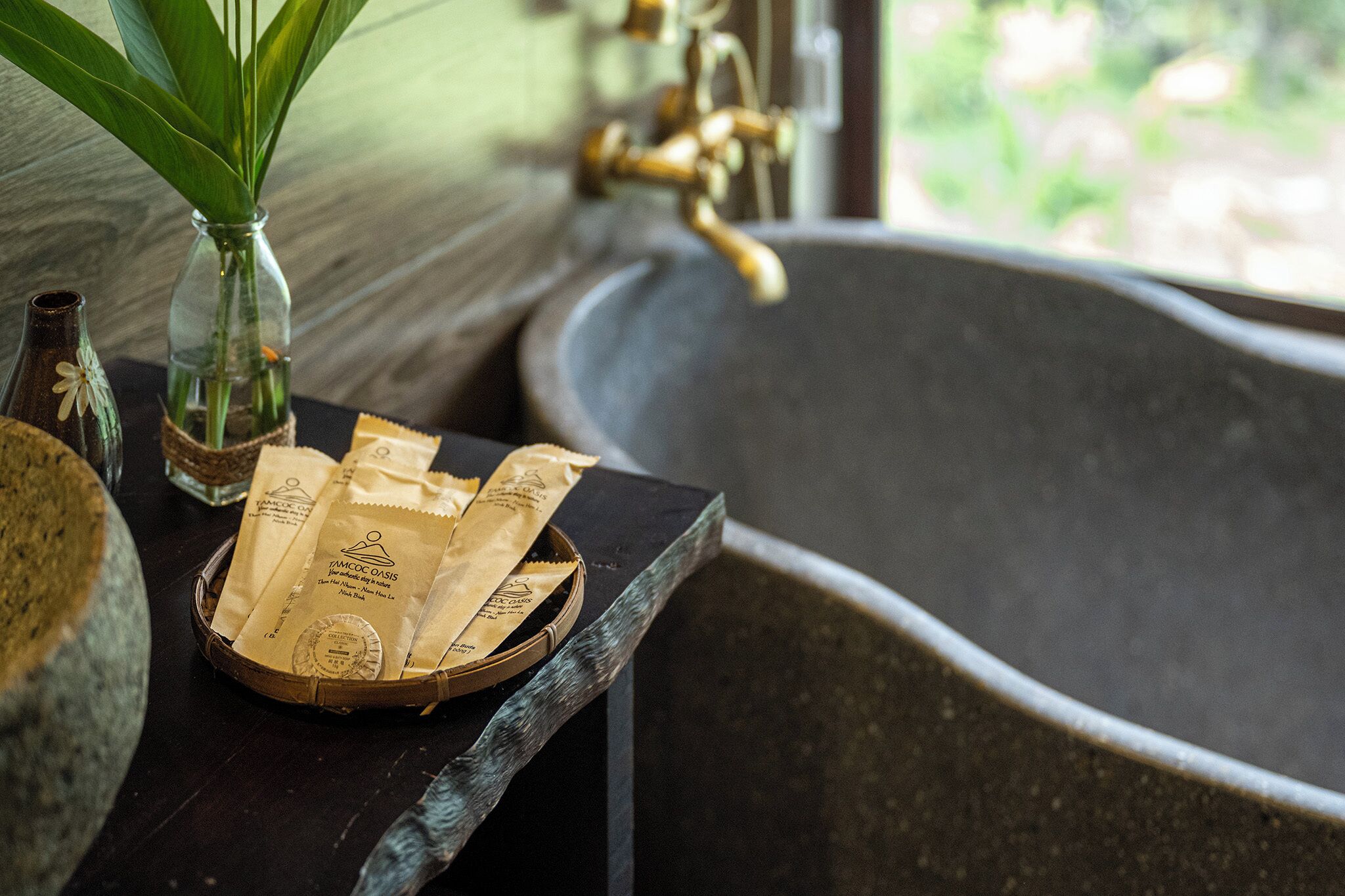 A bathroom with a bathtub, a sink, a vase with green leaves, and a basket of tea bags.