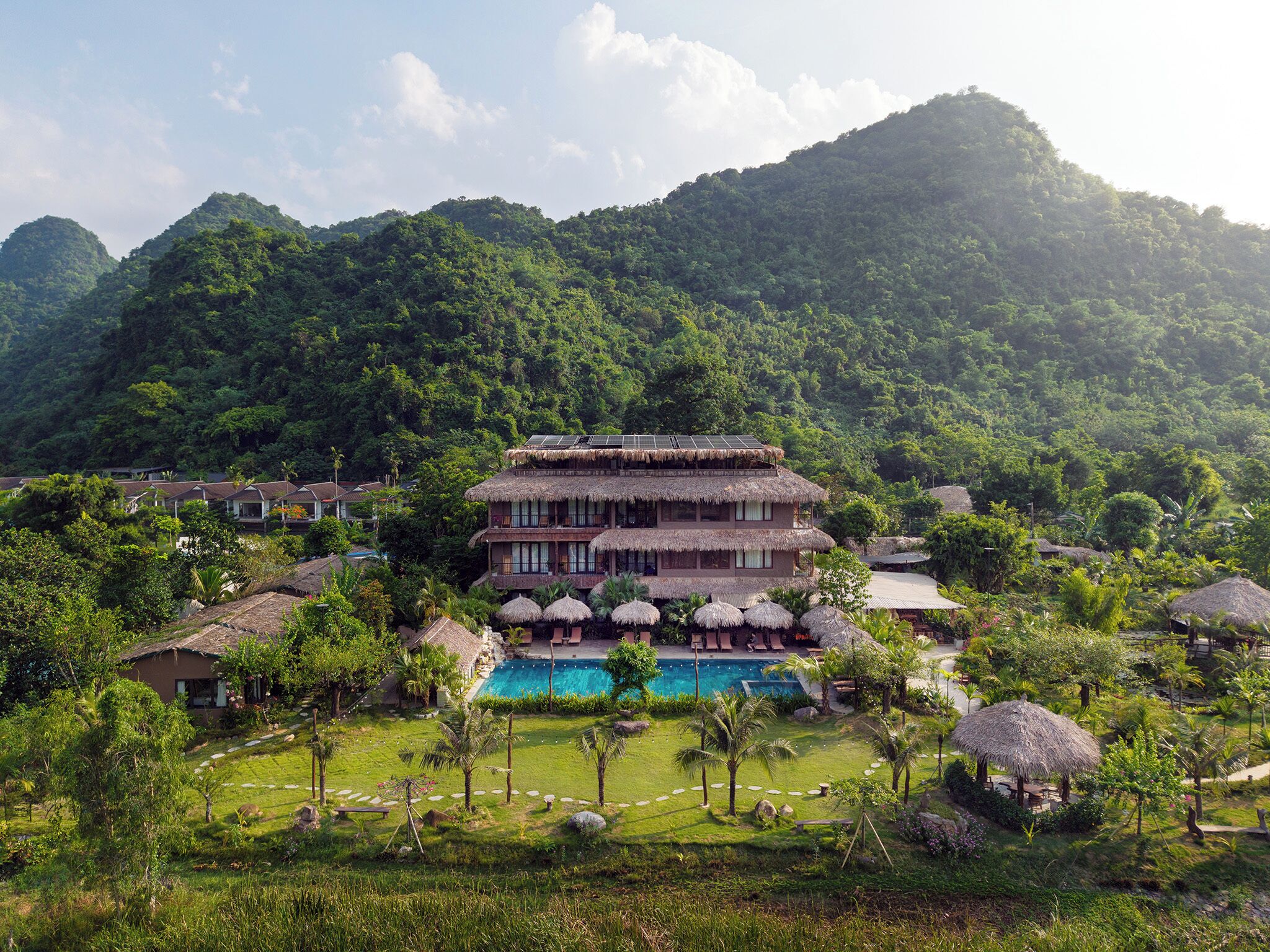 A resort with a pool, thatched-roof structures, and lush greenery.