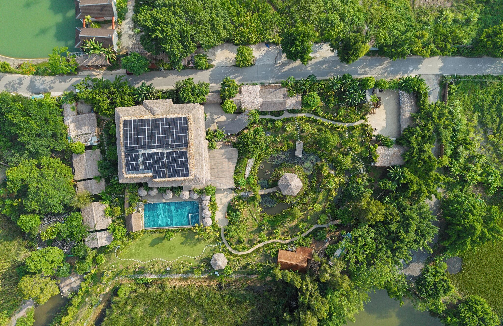 Vista aérea de un resort con piscina, paneles solares y abundante vegetación.