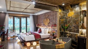 A bedroom with a large bed, a stone wall, a stone fireplace, and a large stone bathtub. - Tam Coc Oasis Resort & Spa (Nam Hoa Lu)