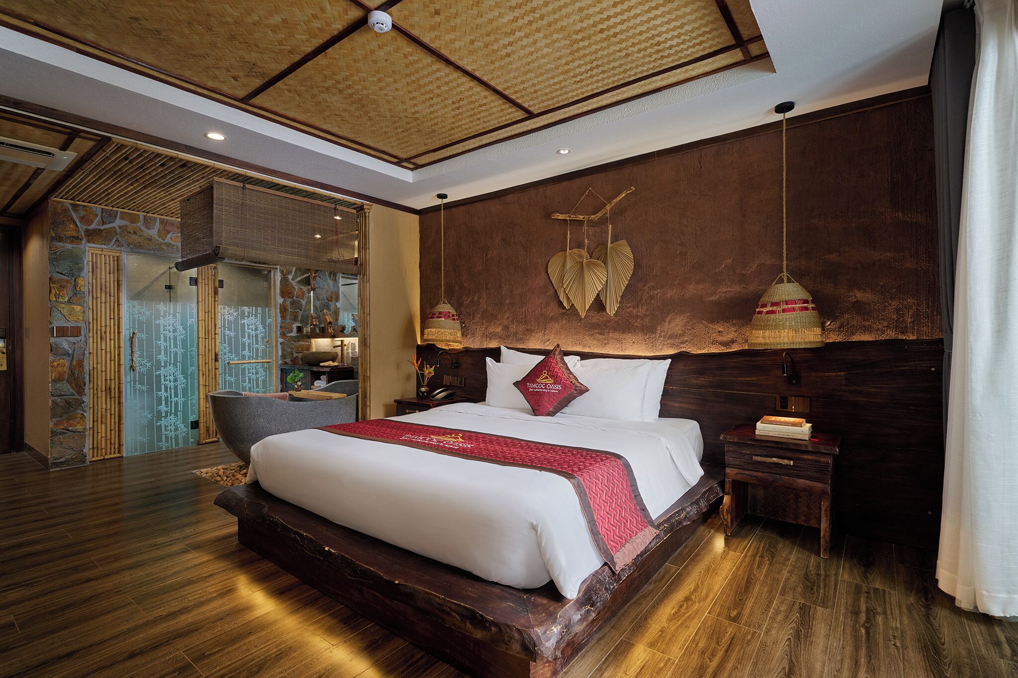 A spacious bedroom with a large bed, wooden headboard, and a view of a traditional bamboo structure.