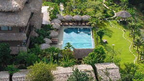 A resort with a swimming pool surrounded by thatched-roof structures and lush greenery. - Tam Coc Oasis Resort & Spa (Nam Hoa Lu)