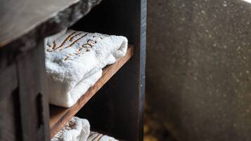 A wooden shelf with white towels, a bathtub, and a stone wall.